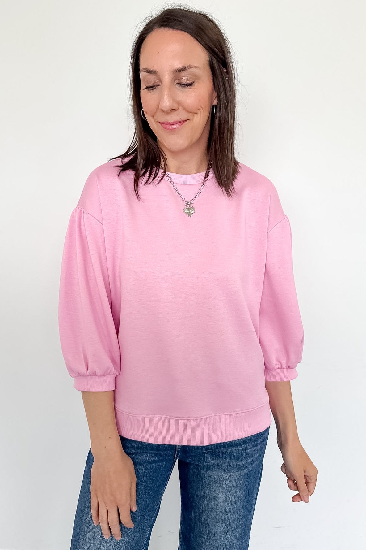 Woman wearing a pink sweatshirt and blue jeans against a white background