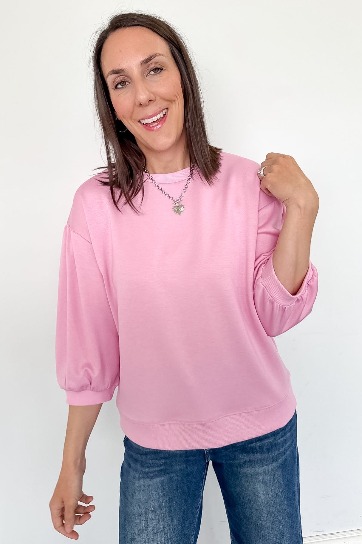 Woman wearing a pink sweater and blue jeans against a white background