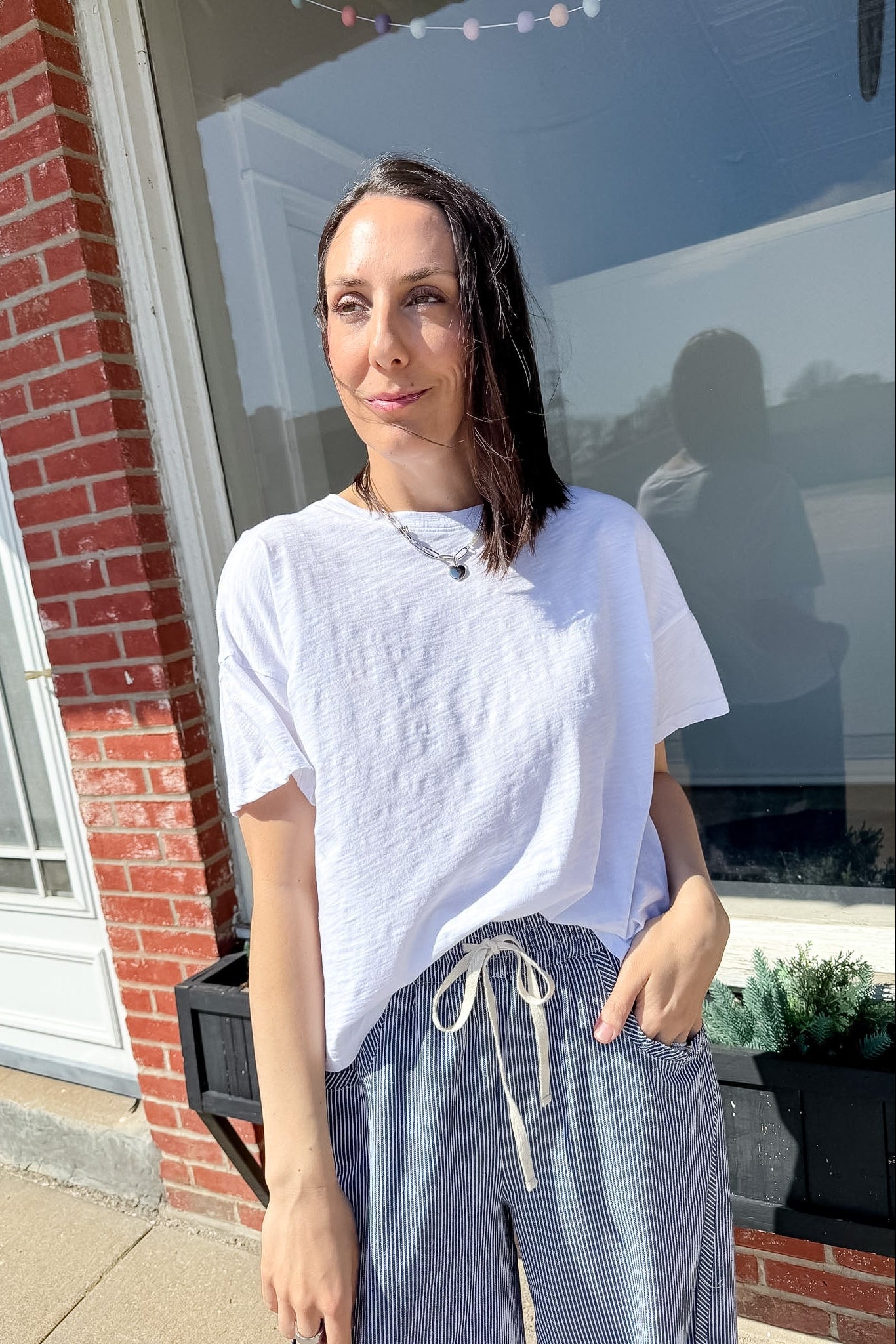 Woman wearing a white t-shirt and striped pants standing outside a building.