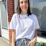 Woman standing outside a house wearing a white t-shirt and striped pants.