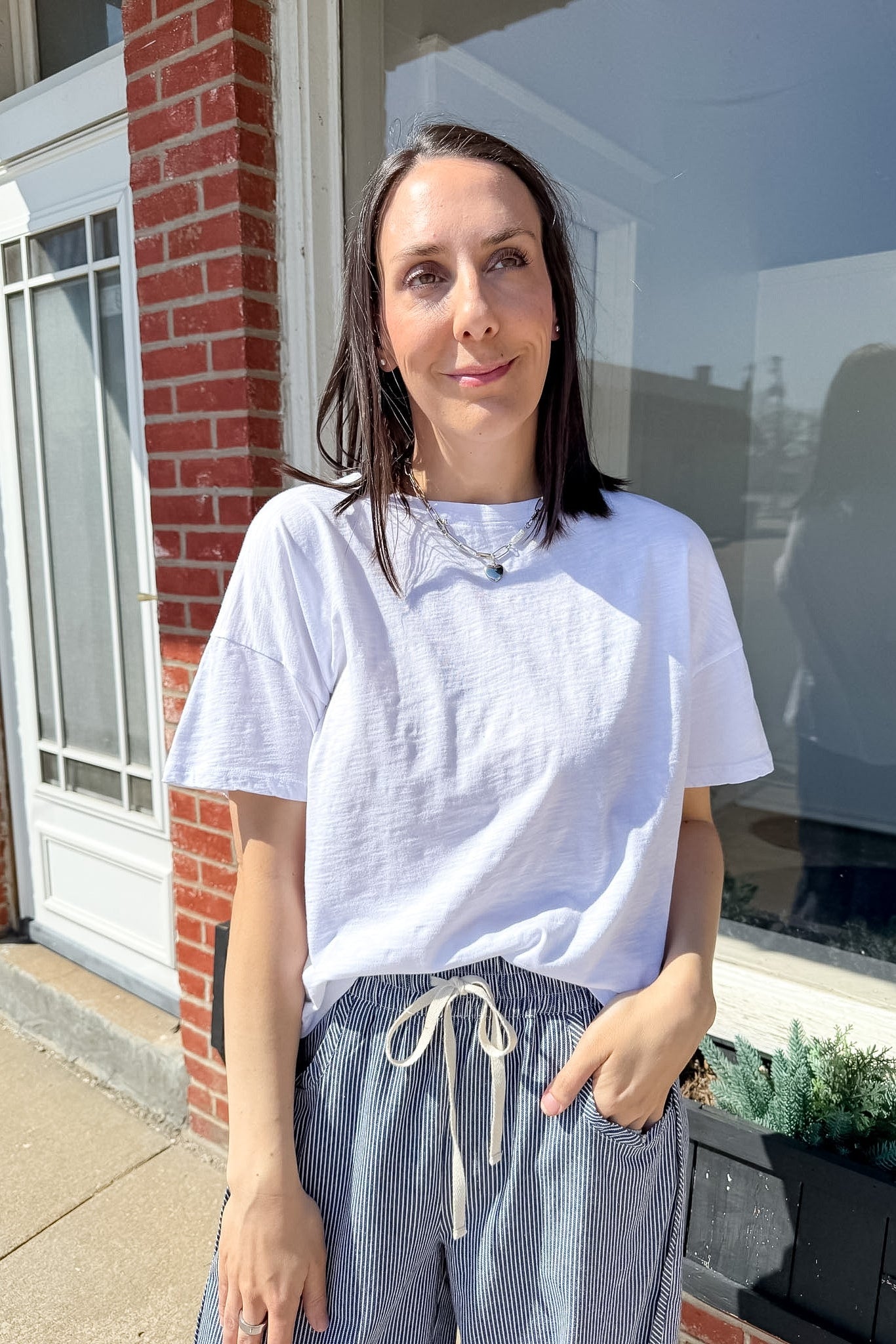 Woman standing outside a house wearing a white t-shirt and striped pants.
