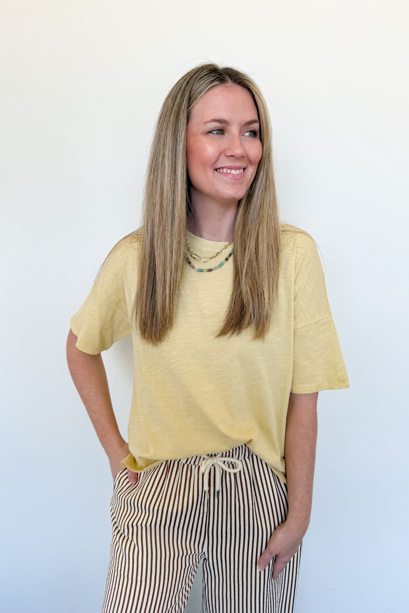 Woman wearing a yellow shirt and striped pants against a white background