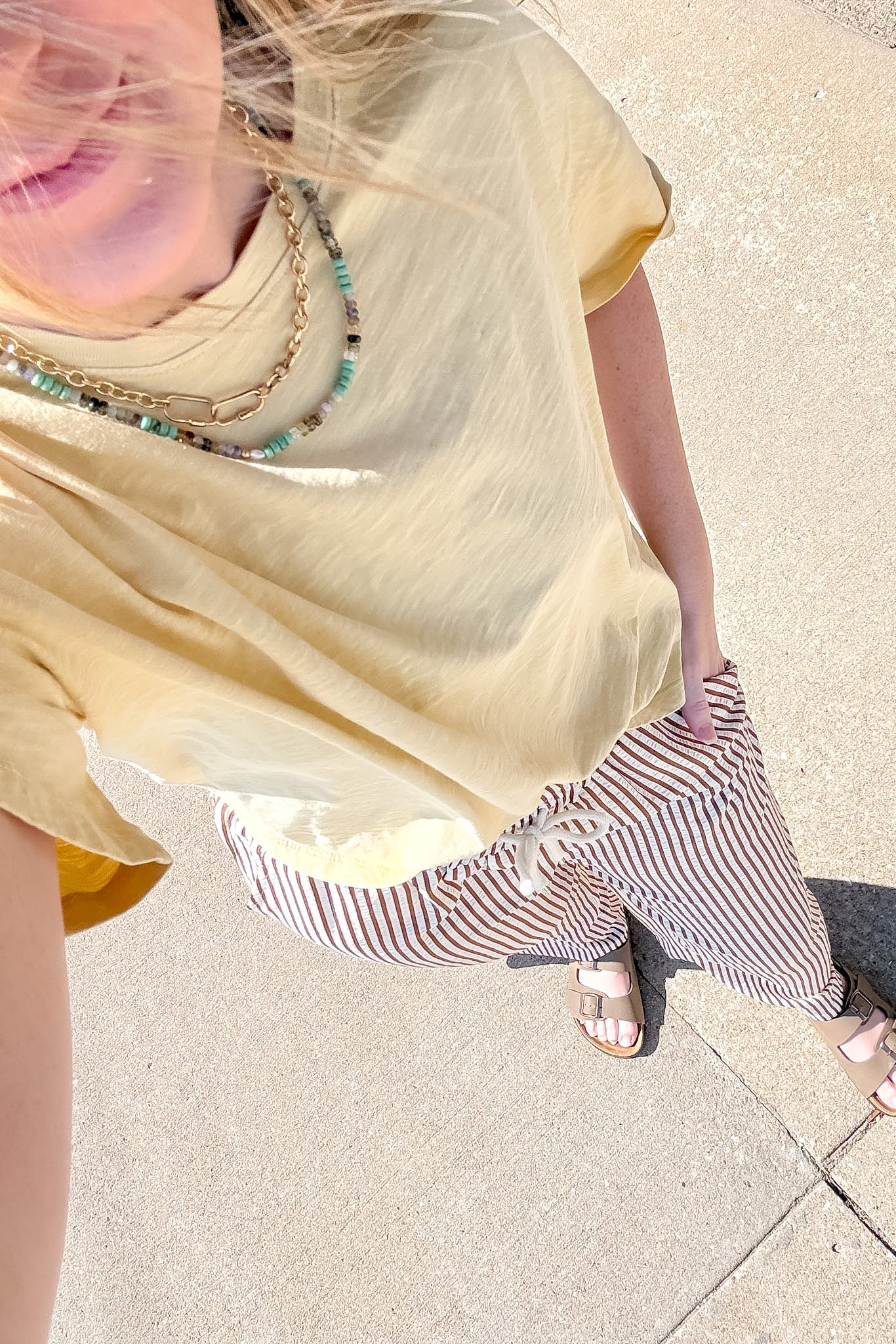 Person wearing a yellow top and striped pants on a sidewalk