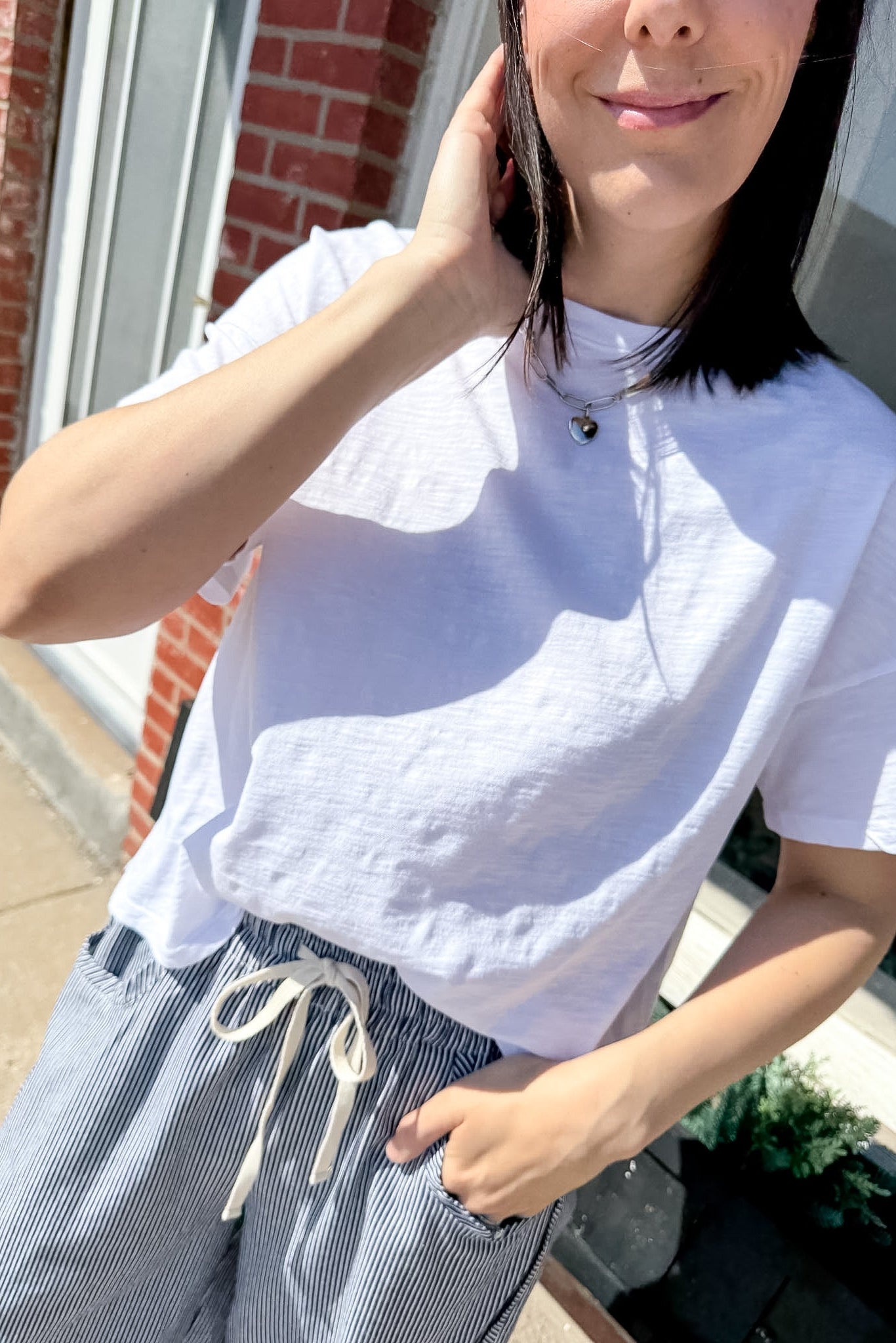 Person wearing a white textured shirt and blue striped pants outdoors.