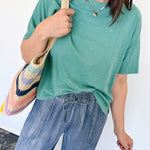 Woman wearing a green t-shirt and blue jeans, holding a colorful bag against a white background