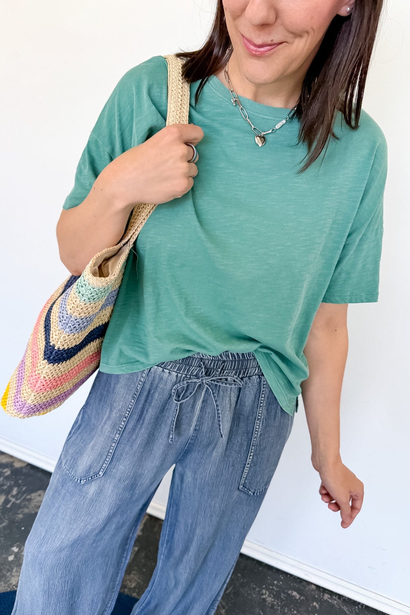 Woman wearing a green t-shirt and blue jeans, holding a colorful bag against a white background