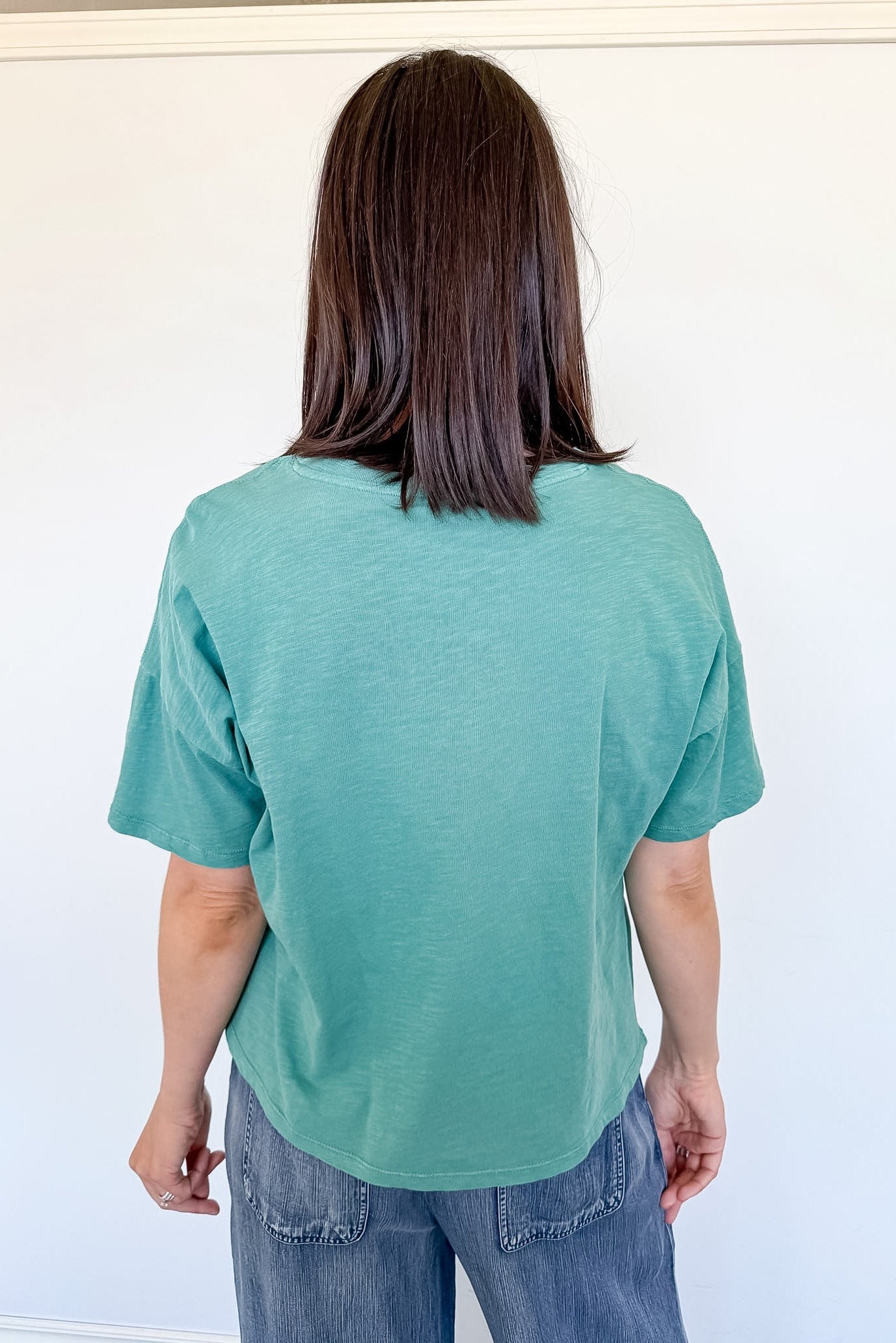 Person wearing a teal t-shirt and blue jeans against a white background