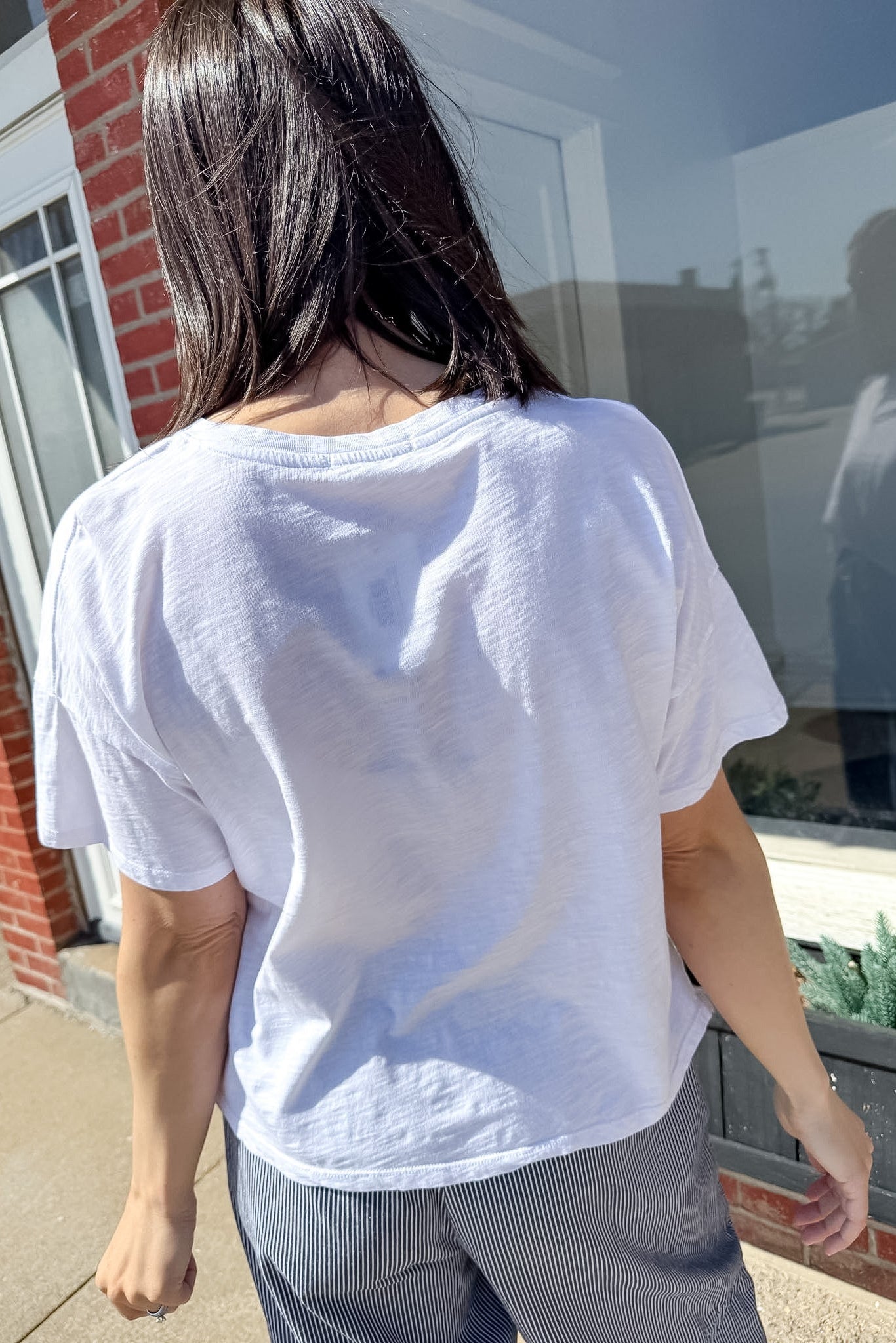 Person wearing a white t-shirt with a visible brand logo, standing outdoors.