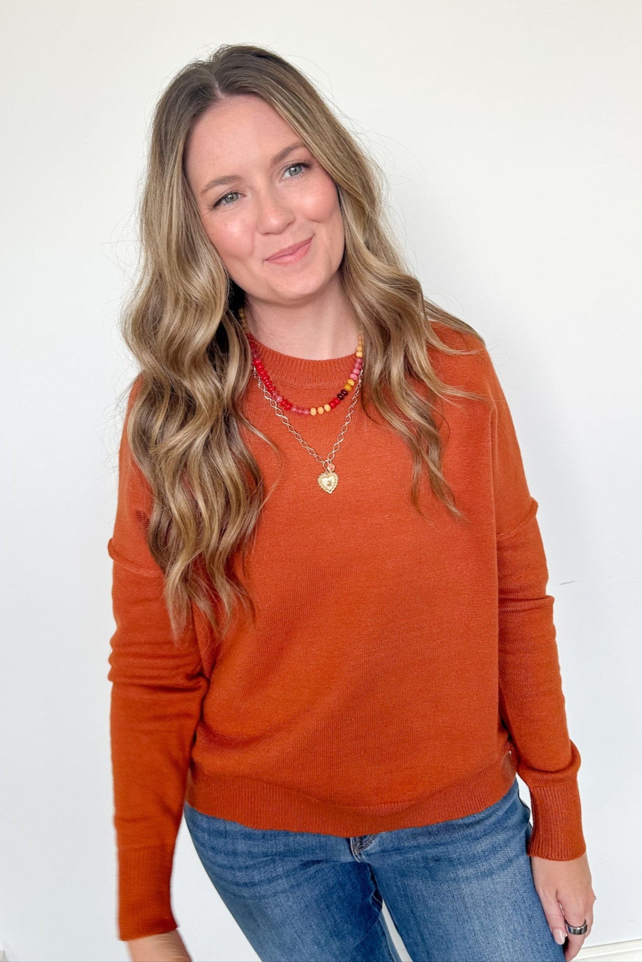 Woman wearing an orange sweater and blue jeans against a white background