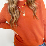 Person wearing an orange sweater and blue jeans with a plain background