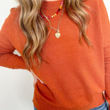 Person wearing an orange sweater and blue jeans with a plain background