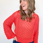 Woman wearing a red lace sweater and blue jeans against a white background