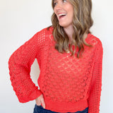 Woman wearing a red lace sweater and blue jeans against a white background