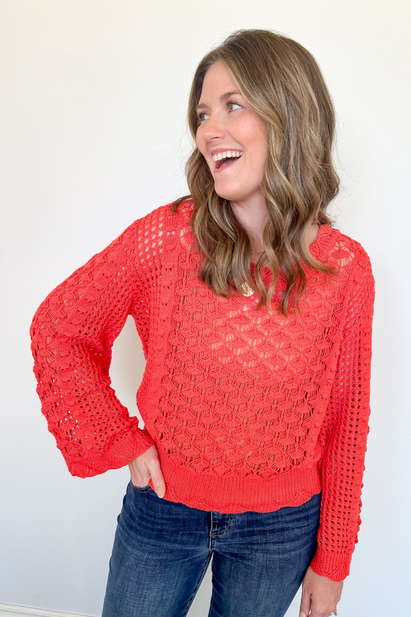 Woman wearing a red lace sweater and blue jeans against a white background
