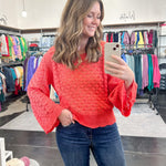 Woman taking a mirror selfie wearing a red sweater and blue jeans in a store.
