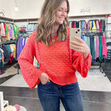 Woman taking a mirror selfie wearing a red sweater and blue jeans in a store.
