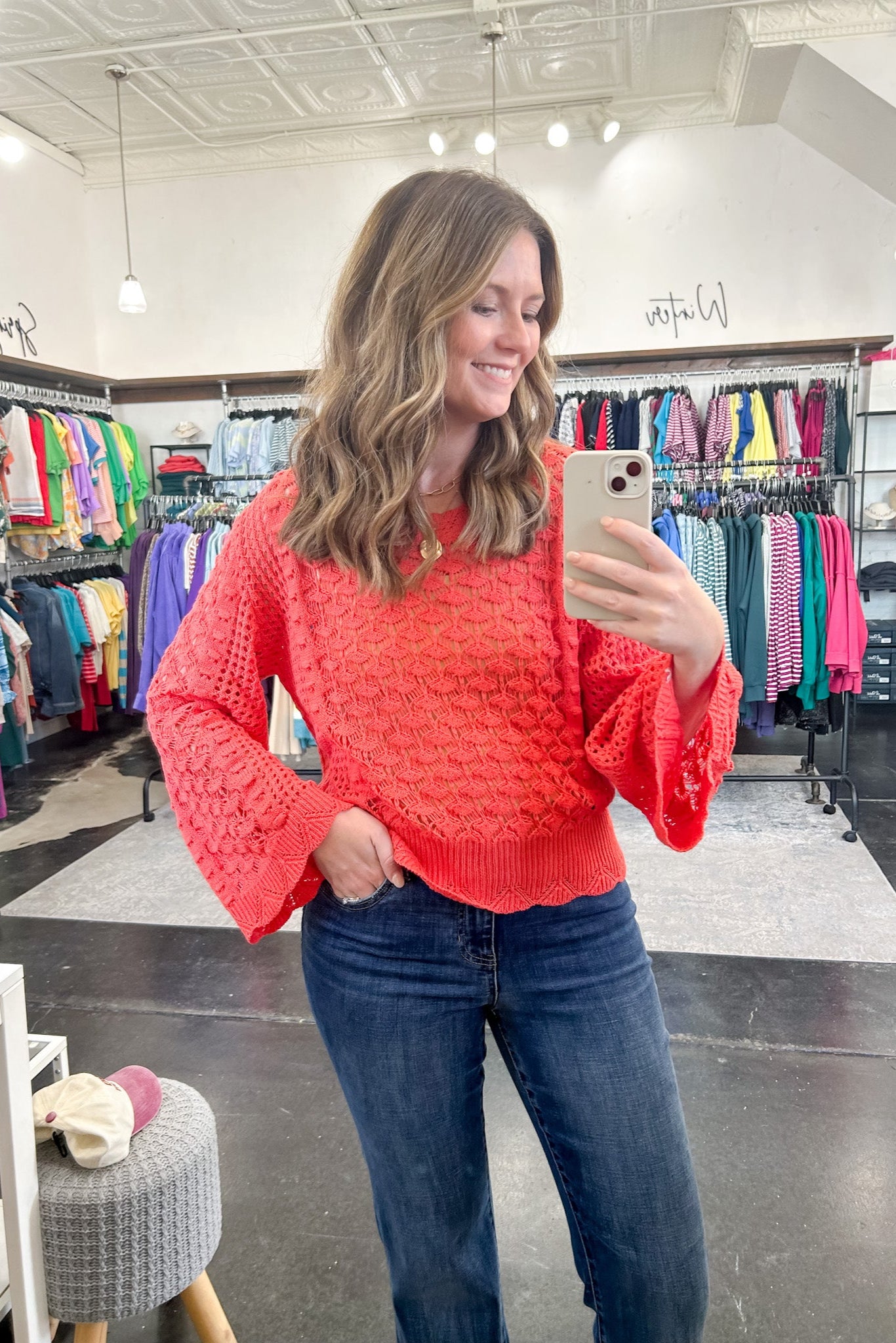 Woman taking a mirror selfie wearing a red sweater and blue jeans in a store.