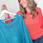 Woman holding a turquoise knitted sweater on a hanger against a white background