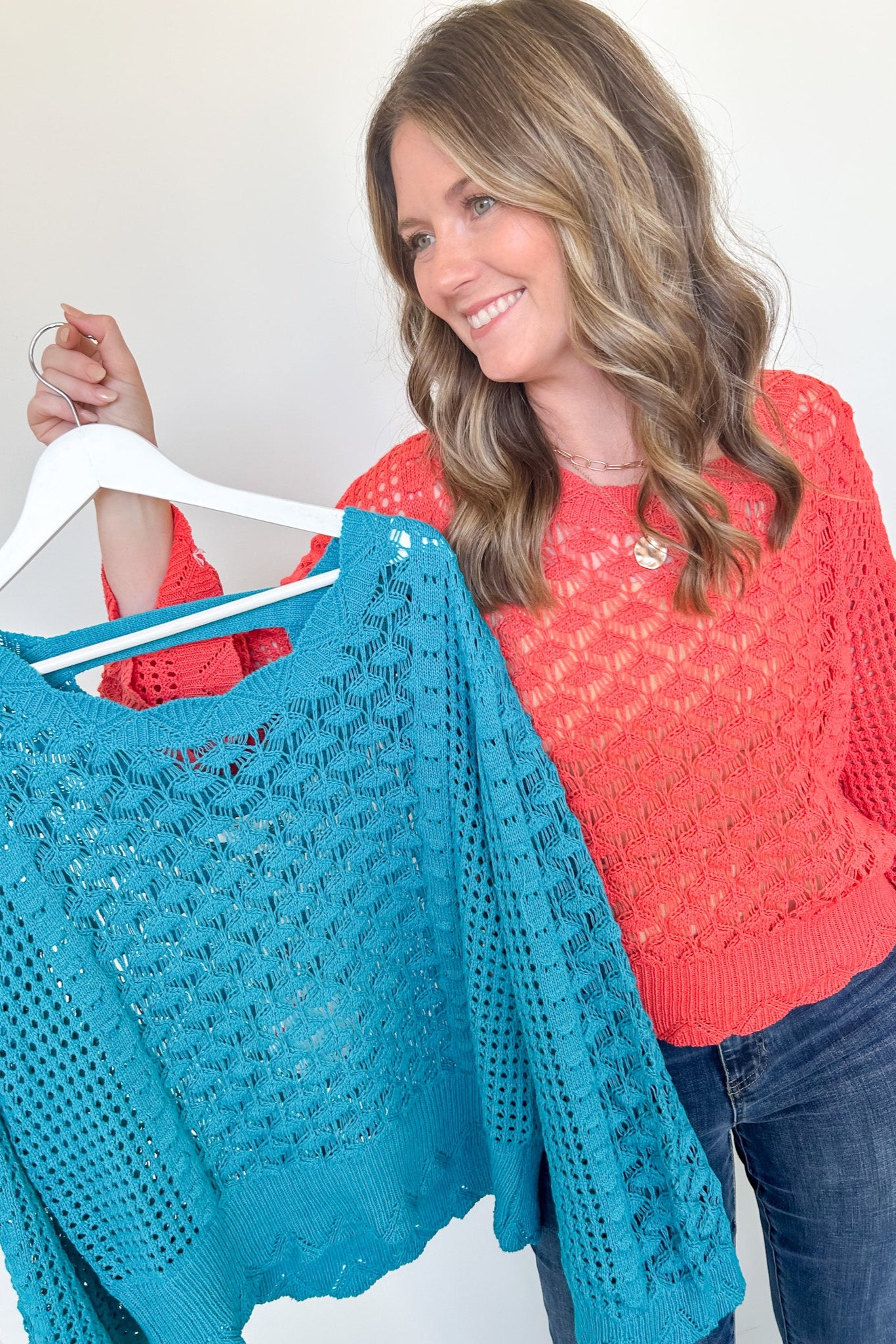 Woman holding a turquoise knitted sweater on a hanger against a white background