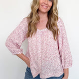 Woman wearing a pink floral blouse and blue jeans against a white background
