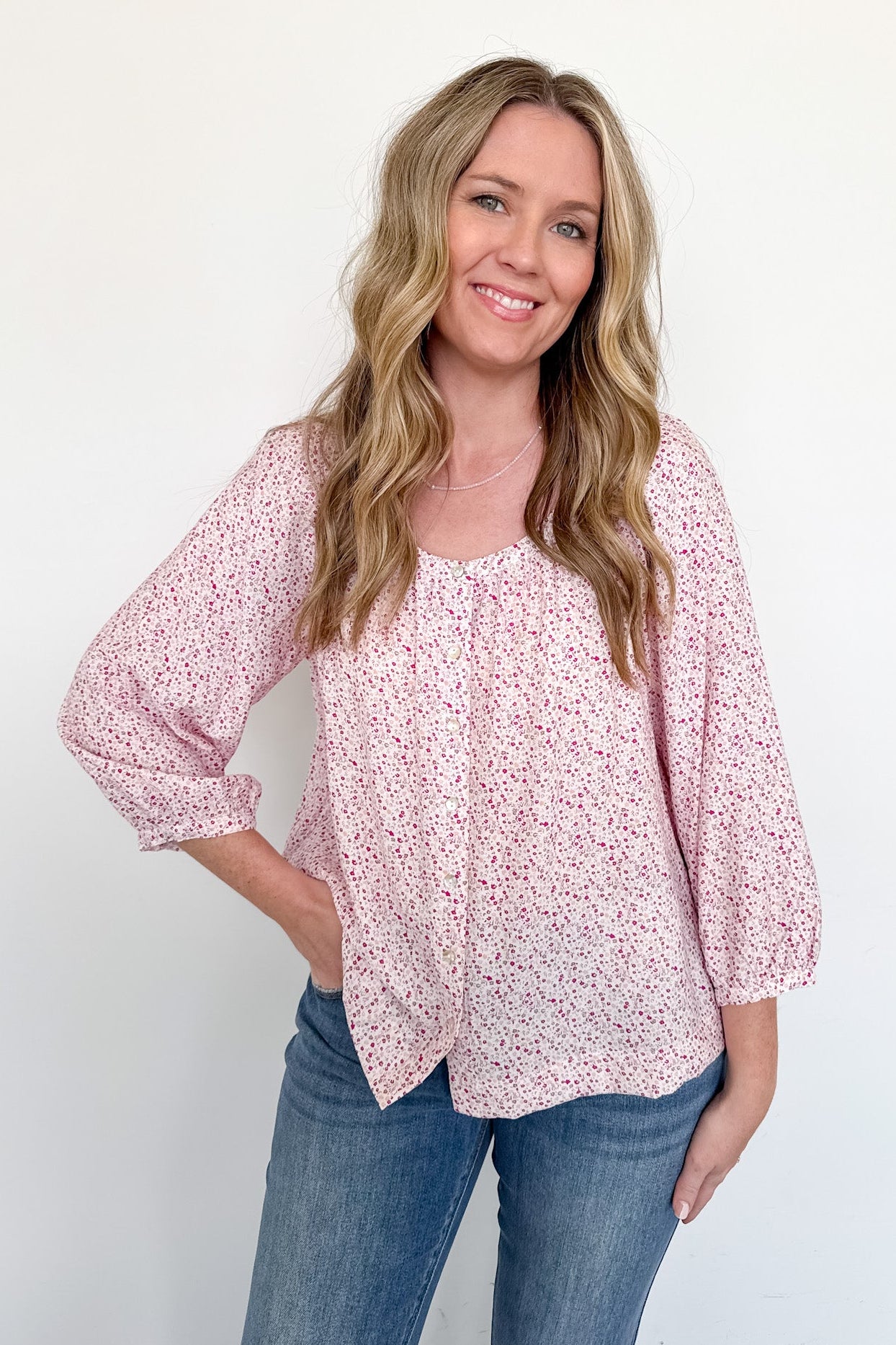 Woman wearing a pink floral blouse and blue jeans against a white background