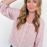 Woman wearing a pink floral blouse and blue jeans, holding sunglasses on a white background