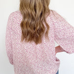 Person wearing a pink floral blouse with long sleeves against a white background