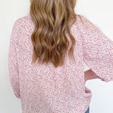 Person wearing a pink floral blouse with long sleeves against a white background