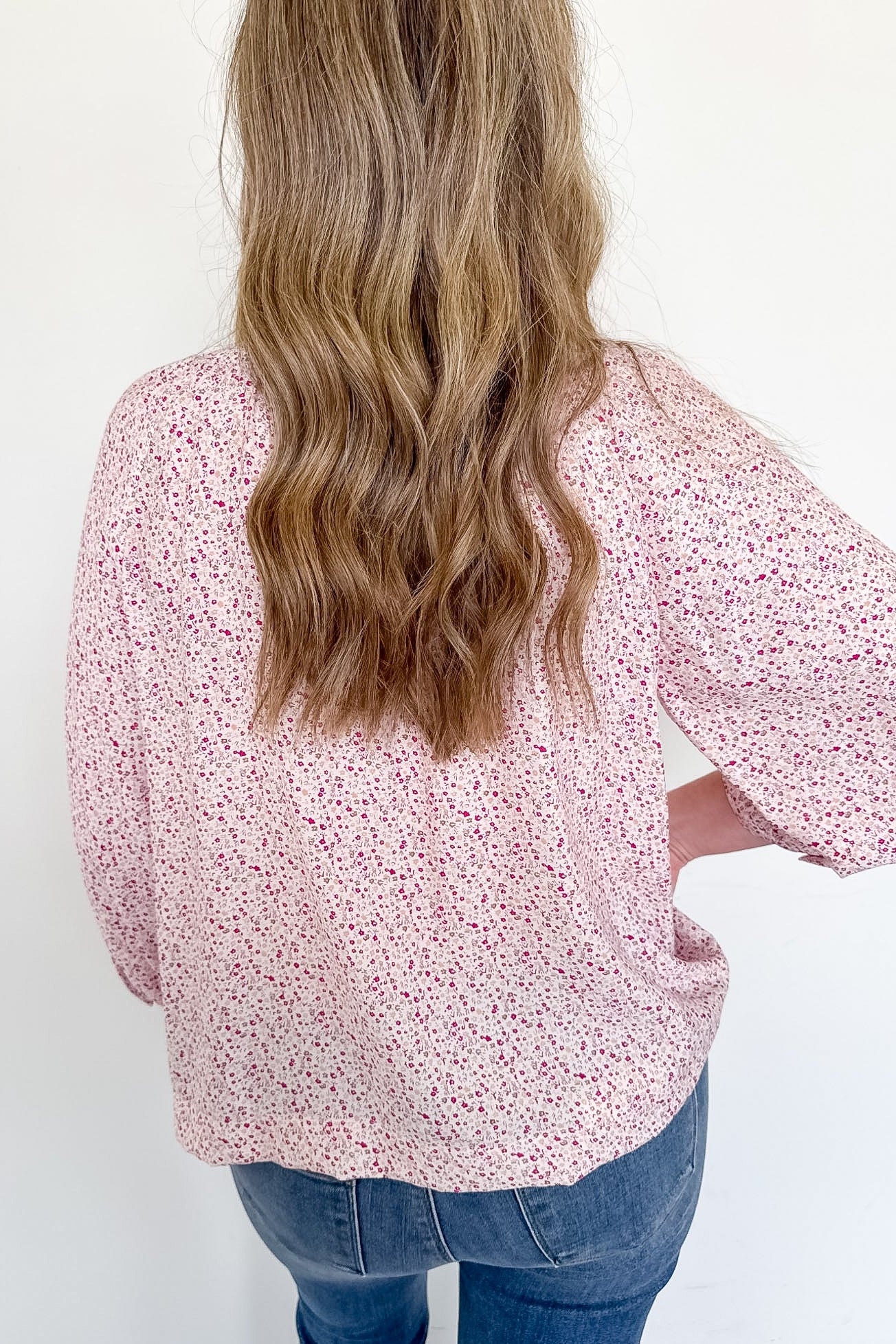 Person wearing a pink floral blouse with long sleeves against a white background