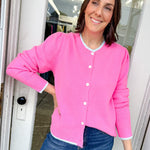 Woman wearing a pink cardigan and blue jeans standing in a doorway.