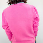Person wearing a bright pink sweater against a white wall