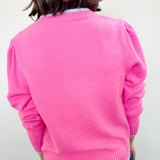 Person wearing a bright pink sweater against a white wall