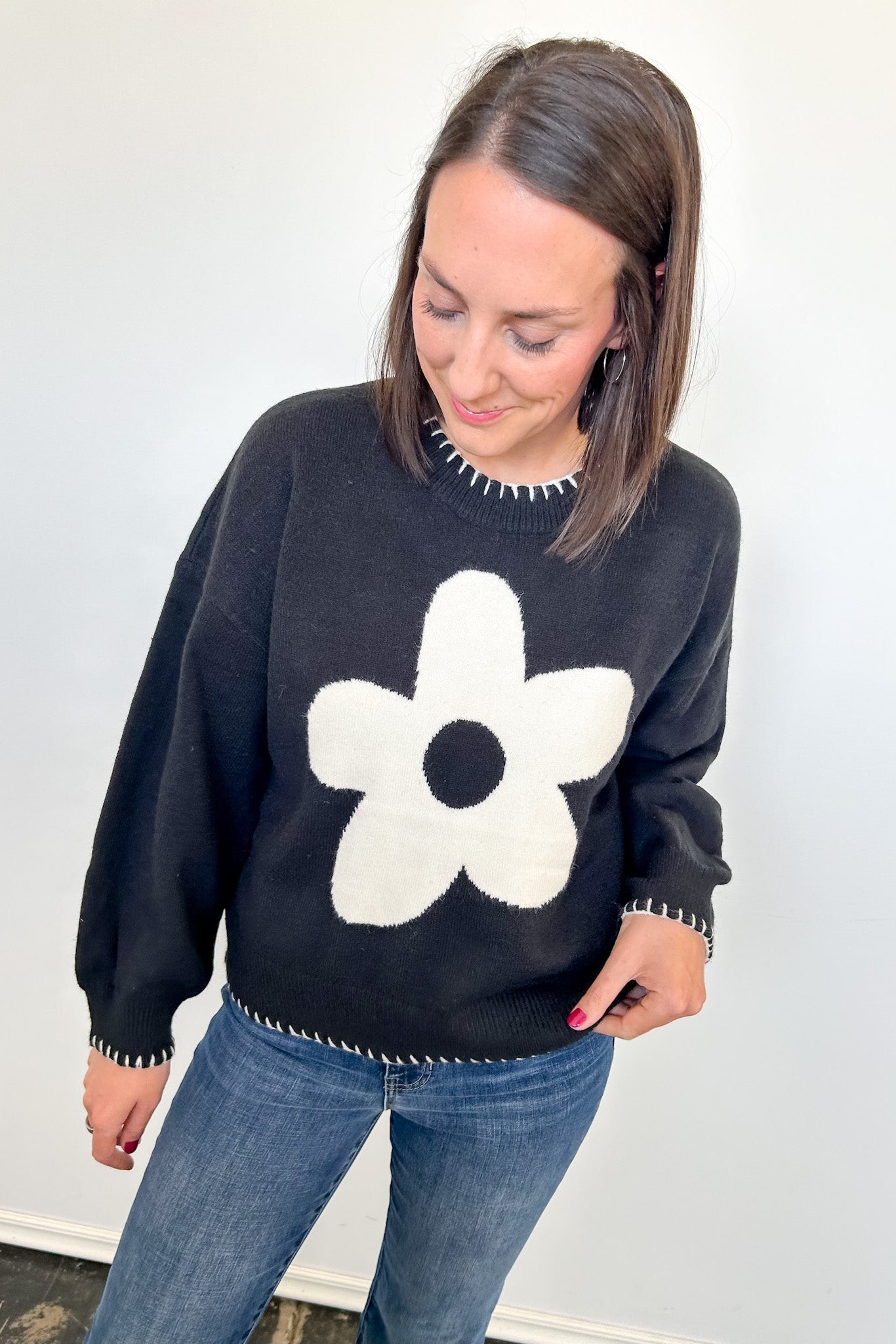 Woman wearing a black sweater with a white flower design against a plain background