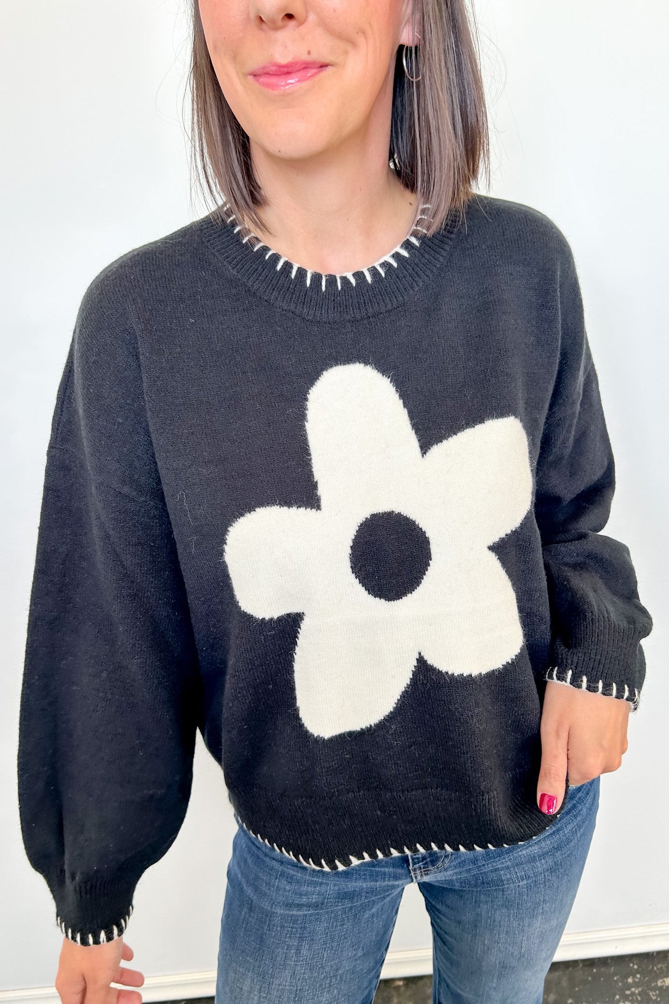Person wearing a dark gray sweater with a white flower design against a plain background