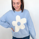 Woman wearing a light blue sweater with a white flower design against a white background