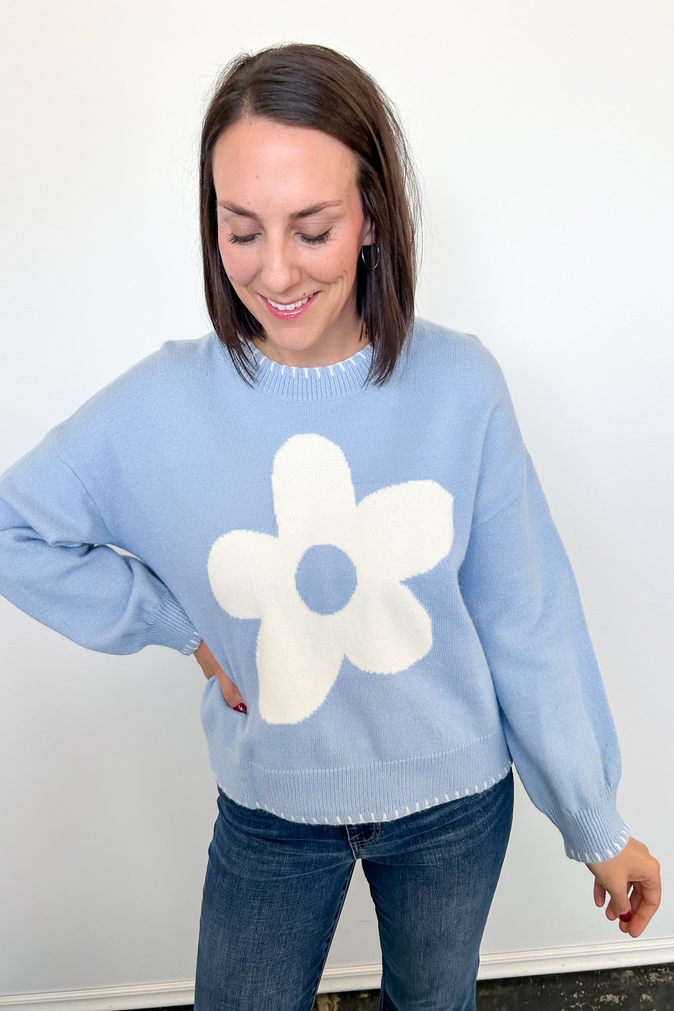 Woman wearing a light blue sweater with a white flower design against a white background