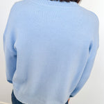 Person wearing a light blue sweater and jeans against a white wall.