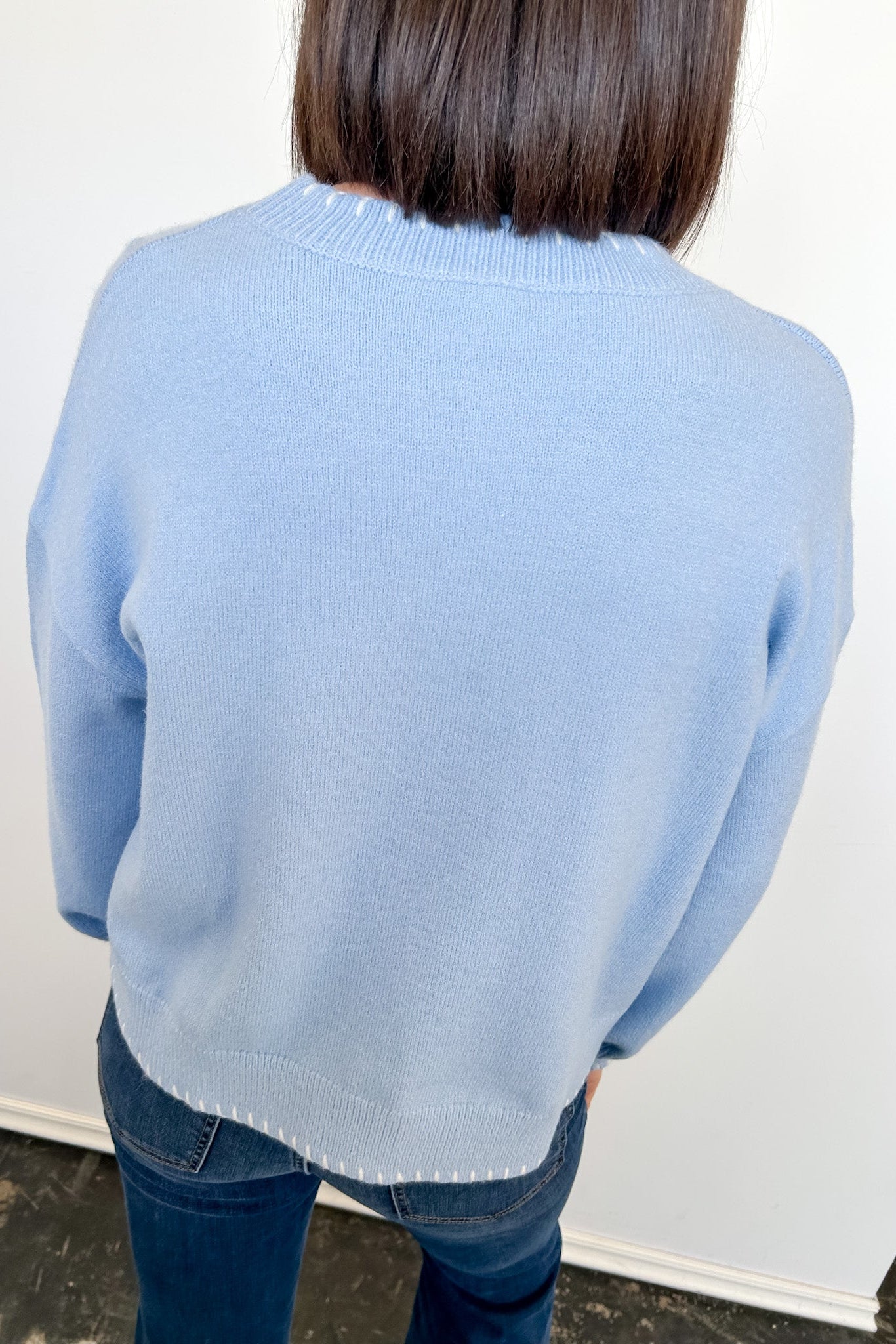 Person wearing a light blue sweater and jeans against a white wall.