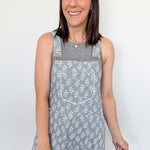 Woman wearing a floral overalls dress against a white wall