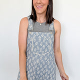 Woman wearing a floral overalls dress against a white wall