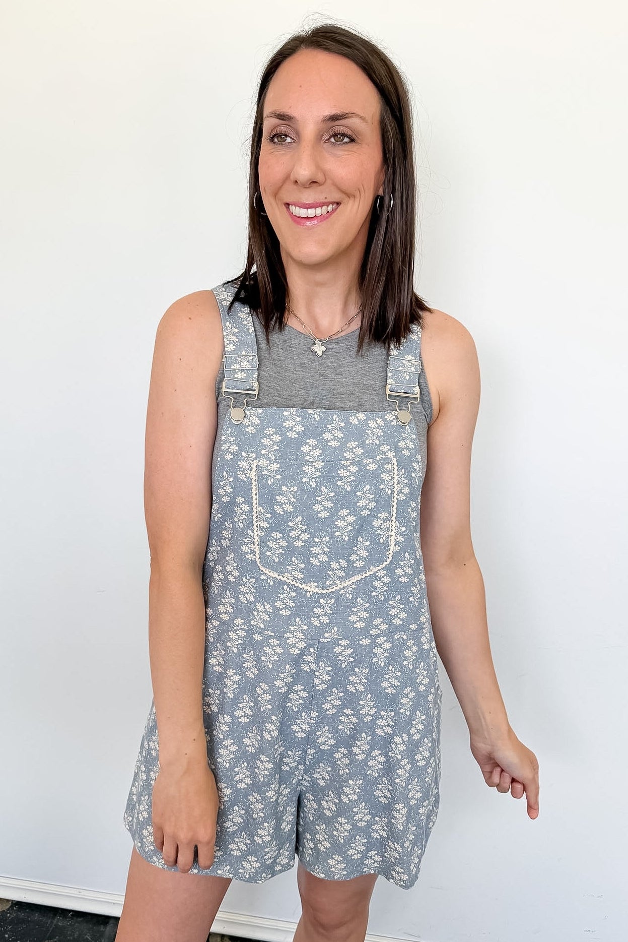 Woman wearing a floral overalls dress against a white wall