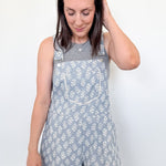 Woman wearing a floral overalls dress against a plain background
