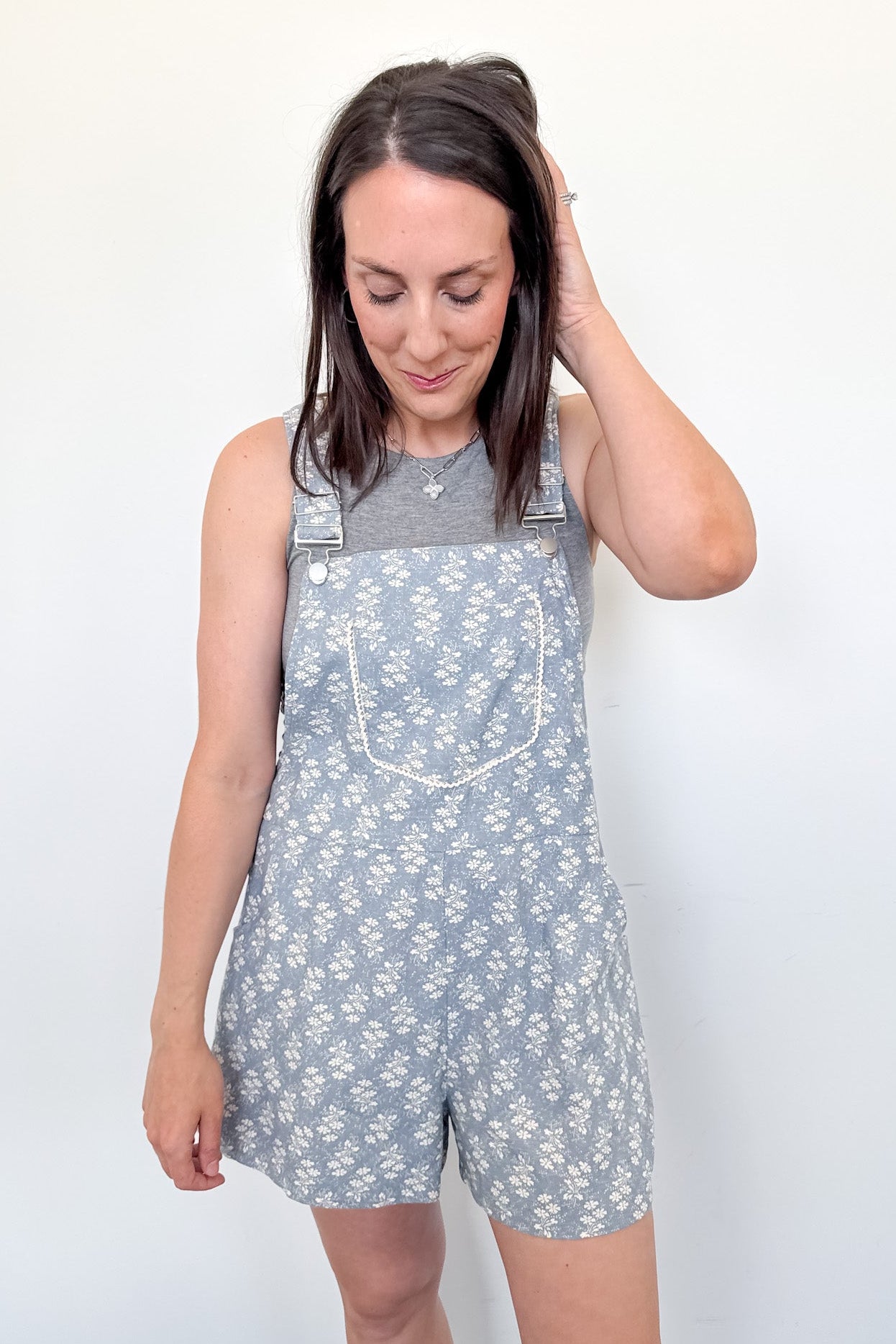 Woman wearing a floral overalls dress against a plain background