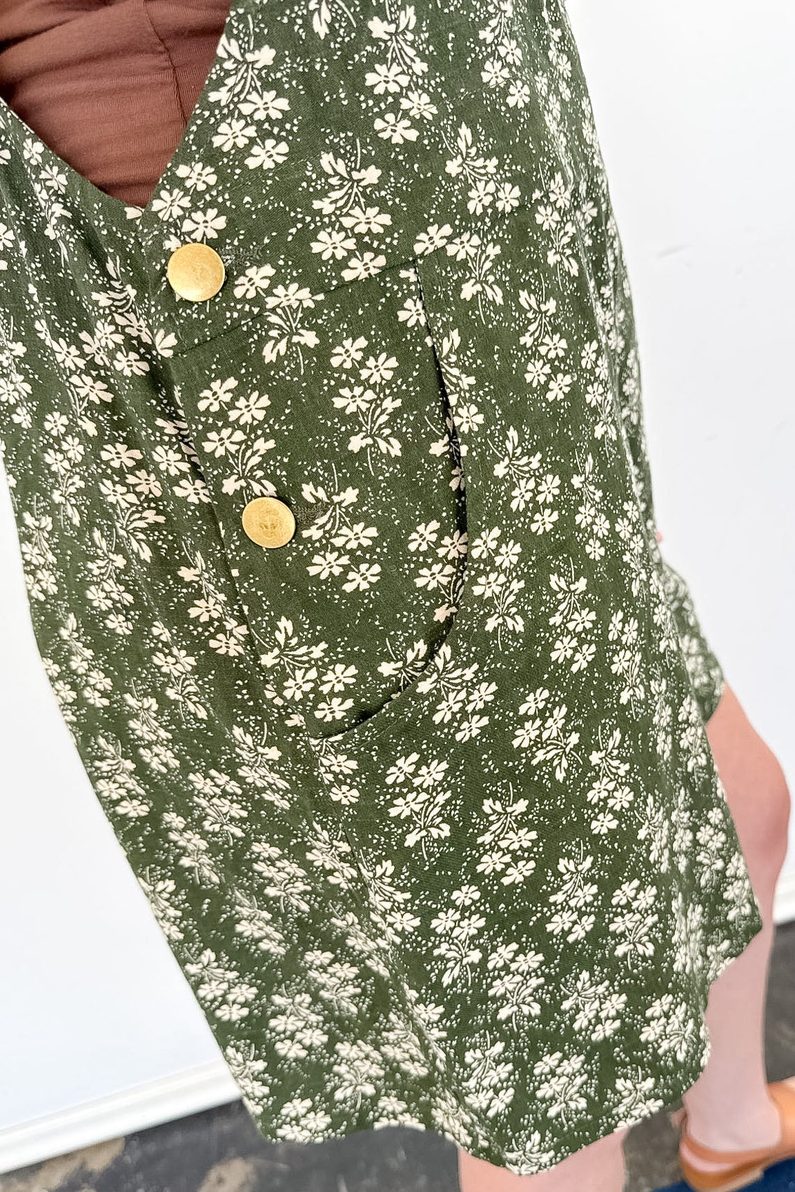 Green floral dress with gold buttons worn by a person on a white background
