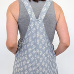 Person wearing a gray floral overalls with a plain background