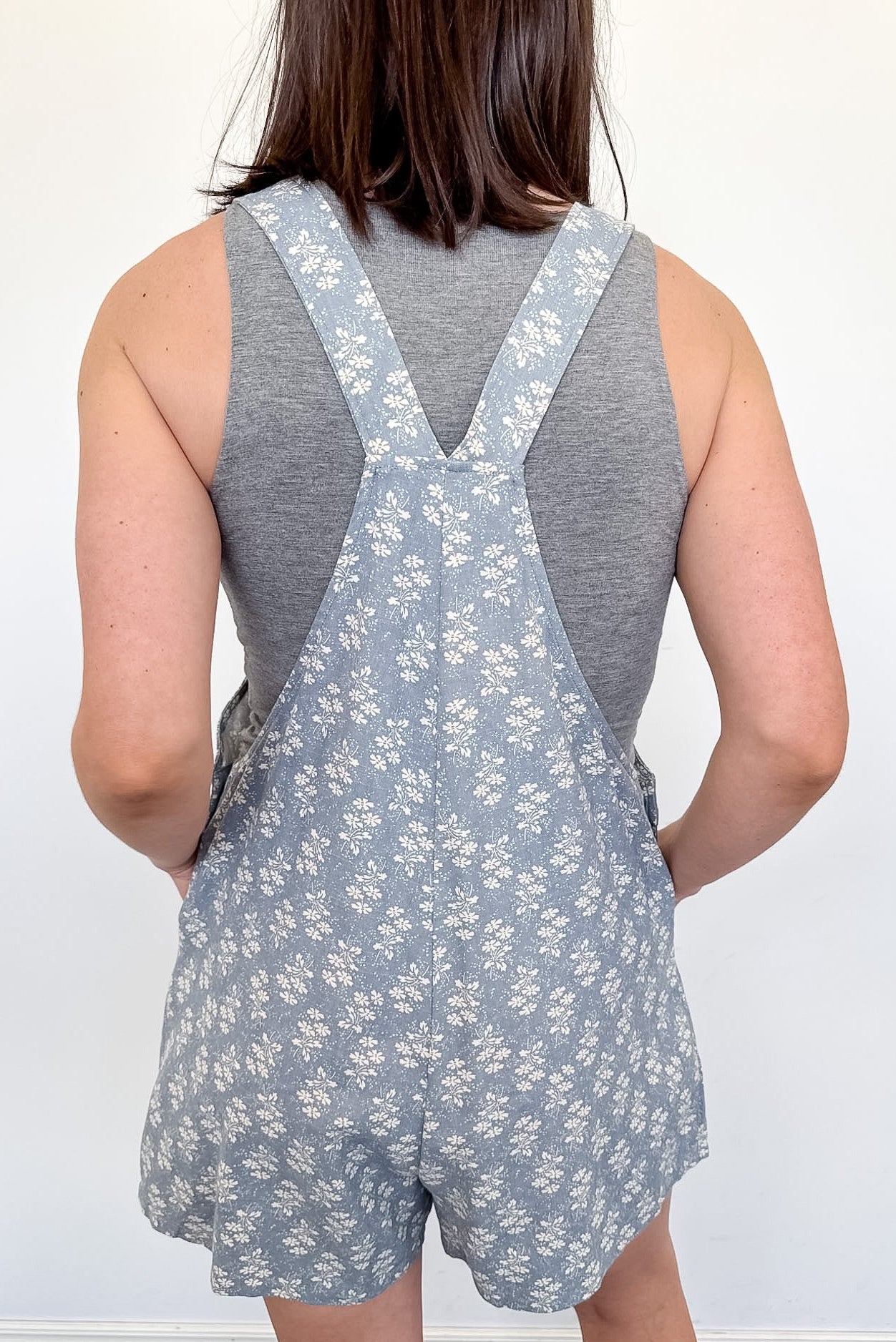 Person wearing a gray floral overalls with a plain background