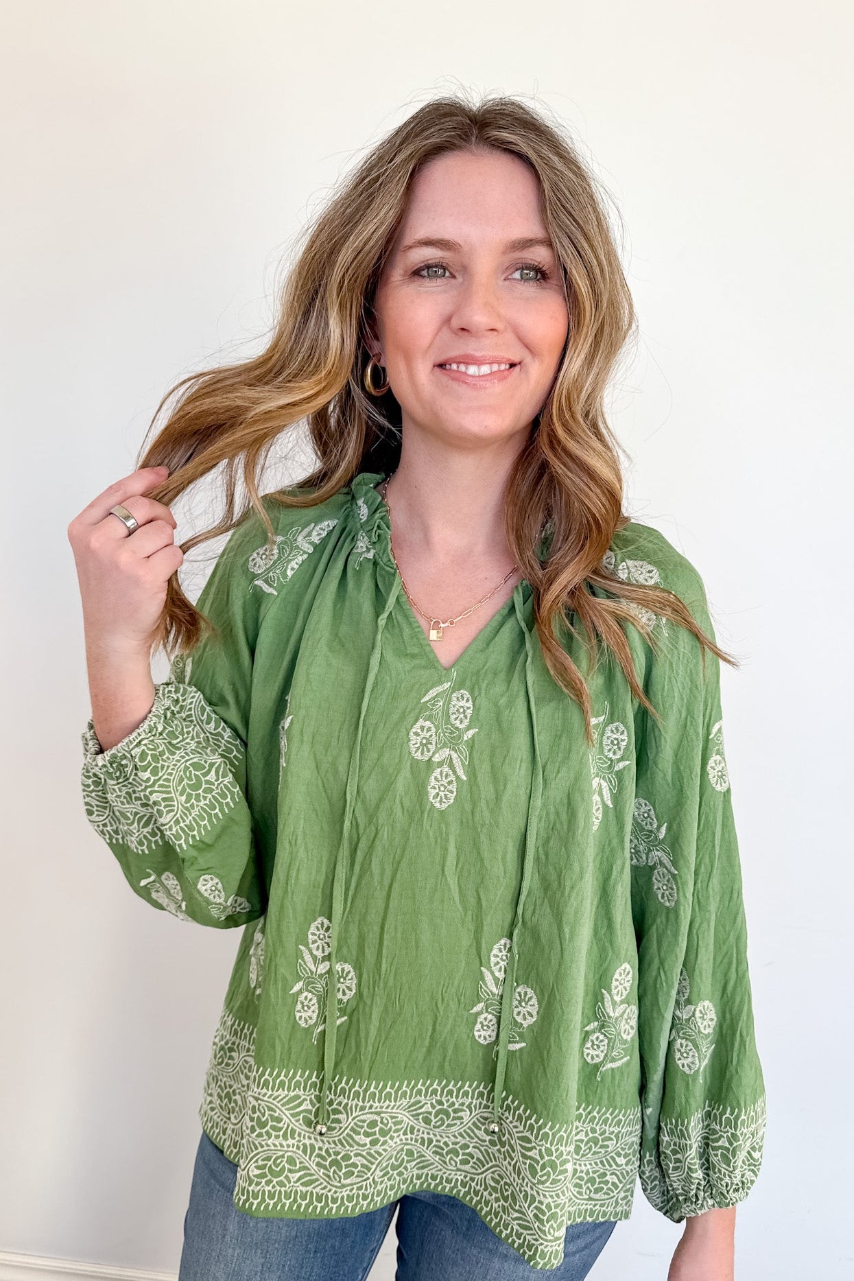 Woman wearing a green embroidered blouse against a white wall