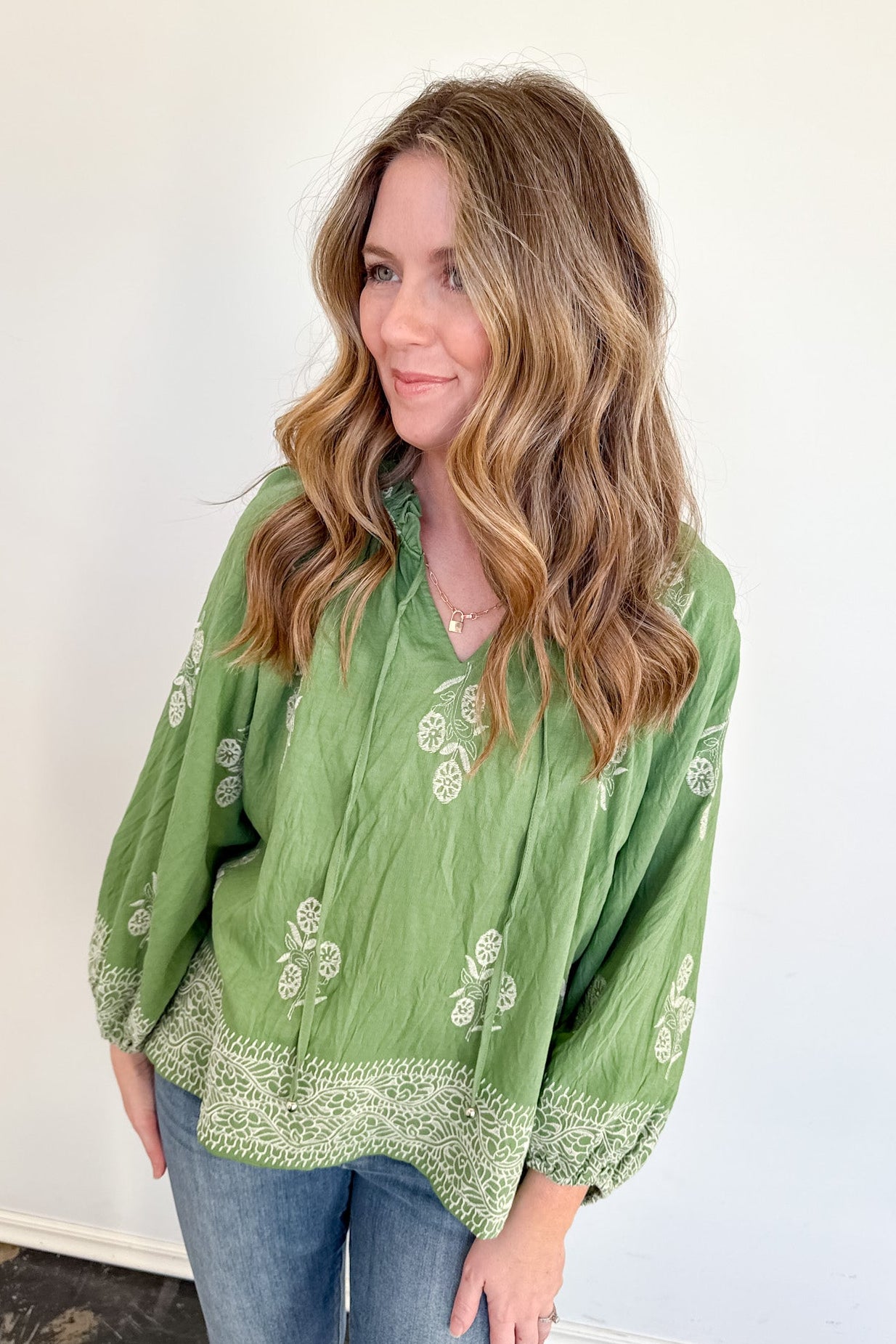Woman wearing a green blouse with white patterns against a white wall.