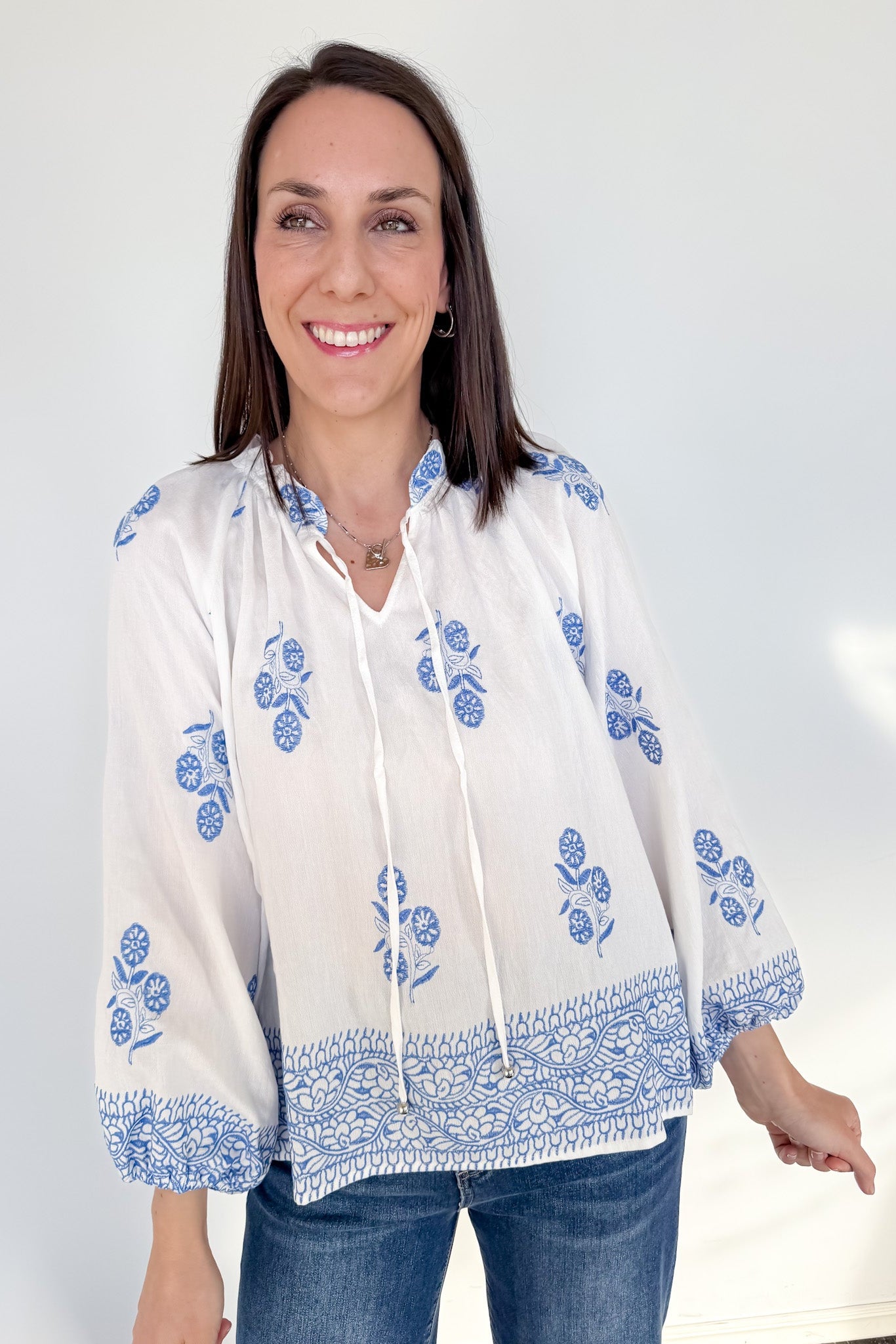 Woman wearing a white blouse with blue embroidery against a white background