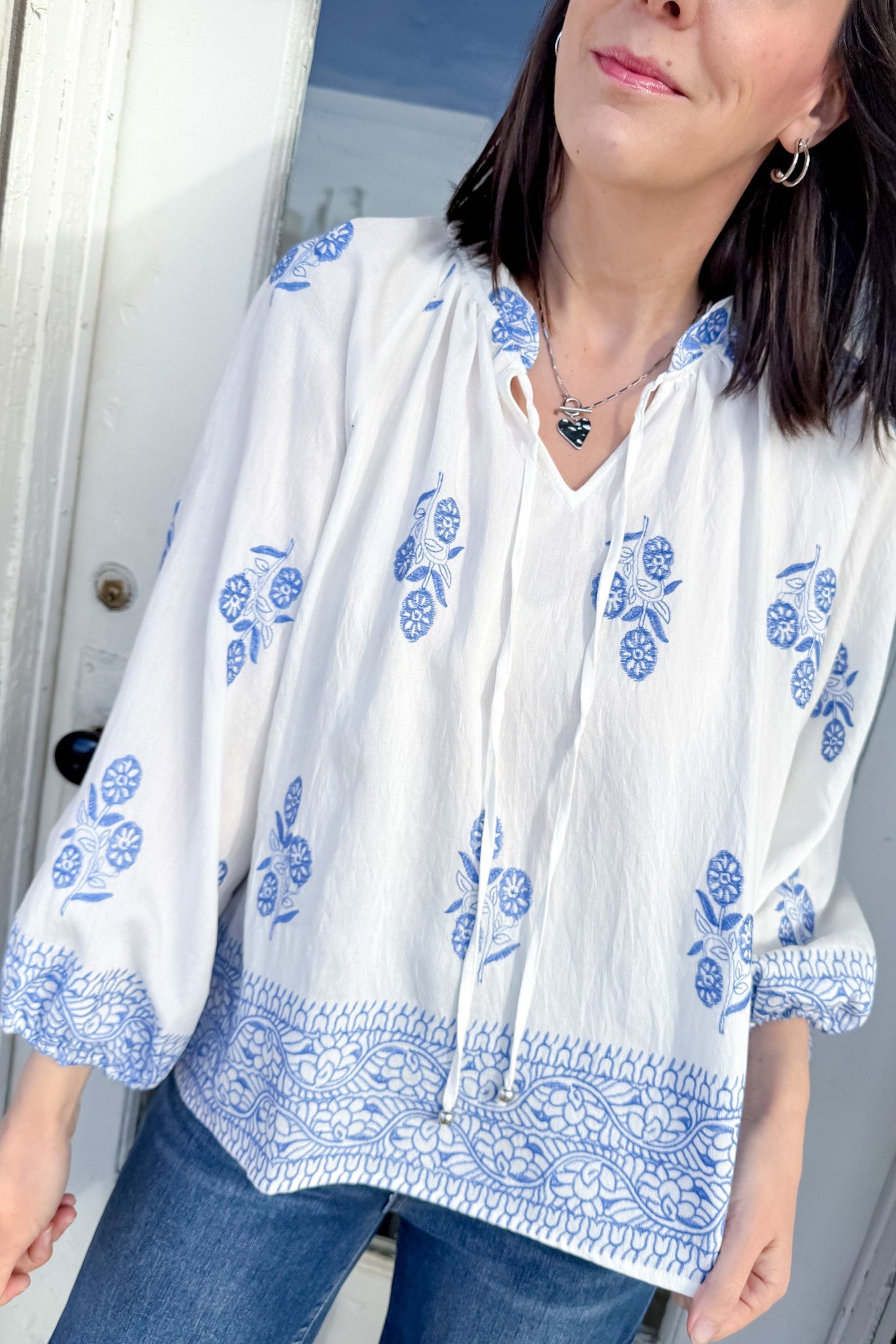 Woman wearing a white blouse with blue floral patterns in front of a white door.